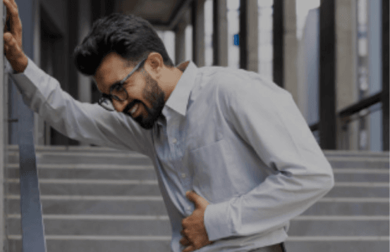 Man experiencing stomach pain and discomfort while holding his abdomen and leaning on a railing outdoors.