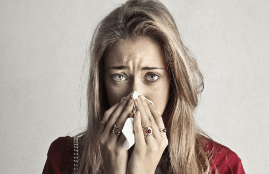 Woman holding a tissue and looking distressed, showing symptoms of cold, flu, or sinus discomfort.
